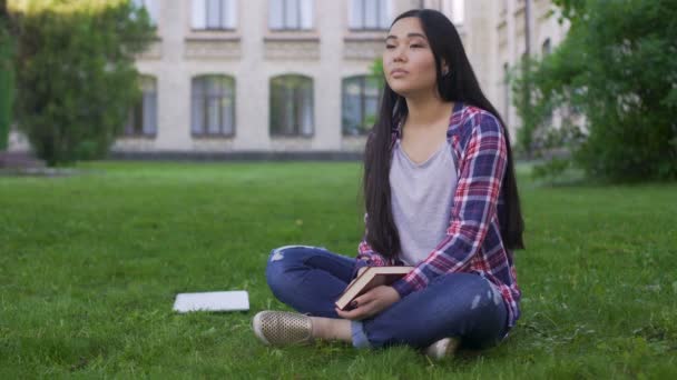 Hermosa chica de raza mixta sentado en el césped cerca de la universidad y soñando con la fecha — Vídeos de Stock