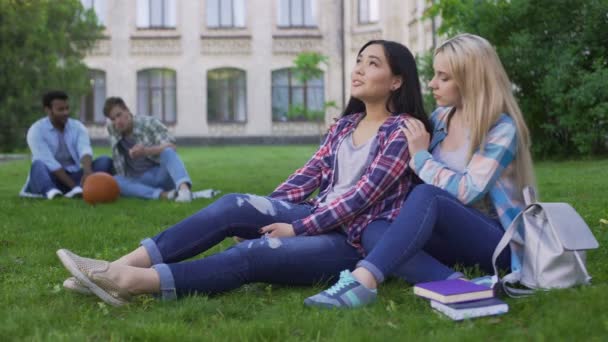 Chica rubia apoyando a su mejor amigo, estudiantes sentados en el césped cerca del campus — Vídeos de Stock