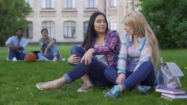 Çimenlikte oturan ve yeni elbiseler, öğrenciler tartışırken oldukça karışık ırk arkadaşlar