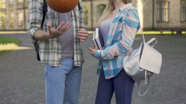 Menina bonita segurando livros e conversando com o homem atlético perto da faculdade, flertar — Vídeo de Stock