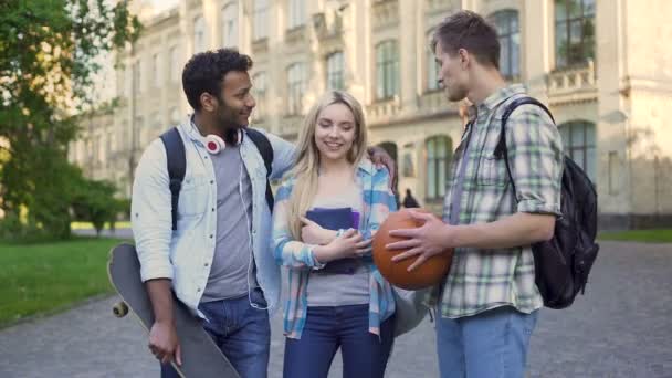 Dos estudiantes masculinos coqueteando con una hermosa chica rubia cerca de la universidad, bromeando — Vídeos de Stock