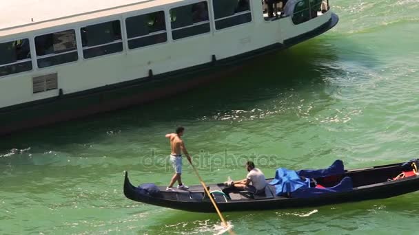 VENICE, ITALY - CIRCA JUNE 2016: Осмотр достопримечательностей города. Молодой гондольер гребная лодка с пассажиром в жаркий летний день, паром проходит мимо — стоковое видео