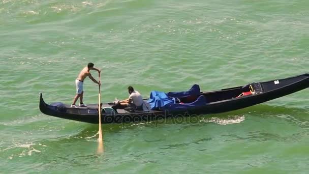 VENICE, ITALY - CIRCA JUNE 2016: Осмотр достопримечательностей города. Гондолье в замедленной съёмке проталкивает гондолу вдоль реки с человеком на борту — стоковое видео