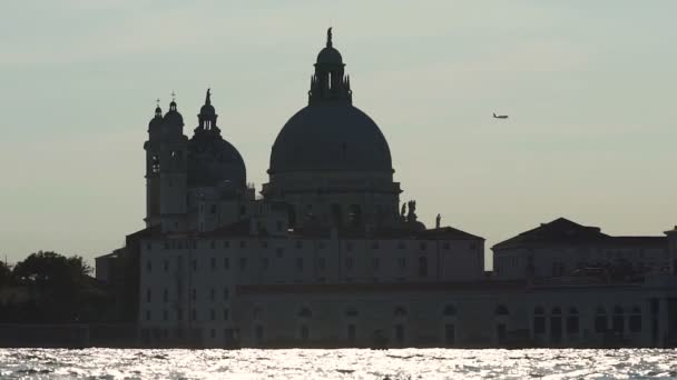 Grande catedral em pé através do rio iluminado pelo sol, avião voando no céu em câmera lenta — Vídeo de Stock