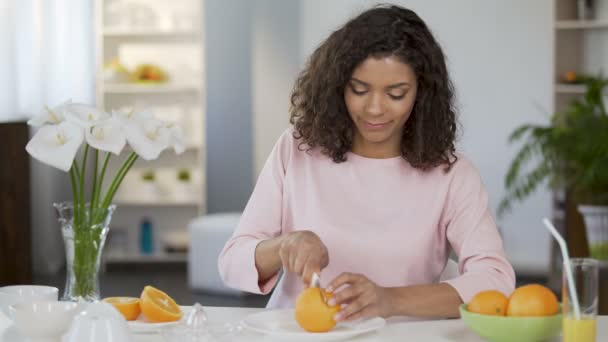 Березовая молодая женщина режет апельсин, улыбается в камеру, здоровый образ жизни — стоковое видео