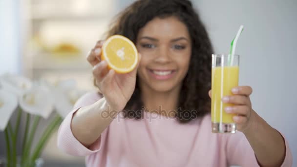 Ung kvinna håller ut orange och glas juice och ler, rik på vitaminer — Stockvideo