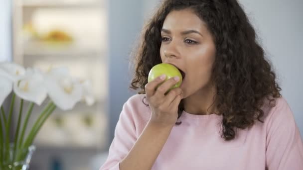 Multirracial bela mulher comendo maçã à mesa, sonhando acordado, pensamentos felizes — Vídeo de Stock