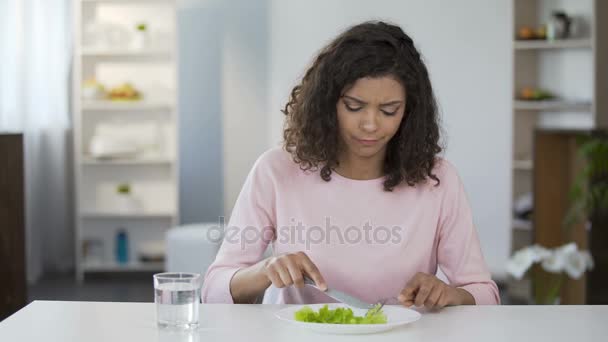 Молодая женщина вынуждает себя есть салат, недовольство, контроль веса, диета — стоковое видео