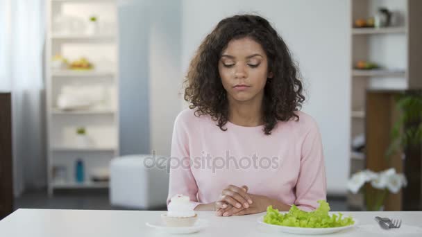 Schöne zweirassige Frau, die zwischen Salat und Süßigkeiten, Gesundheit, Wahl — Stockvideo