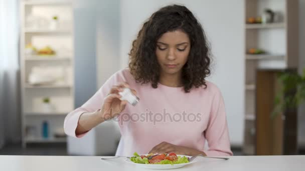 Jeune femme métisse ajoutant trop de sel à la salade et à la nourriture, habitude nocive — Video