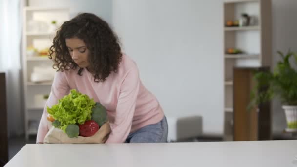 Smíšené rasy mladá žena uvedení zelenina na stole po nakupování — Stock video