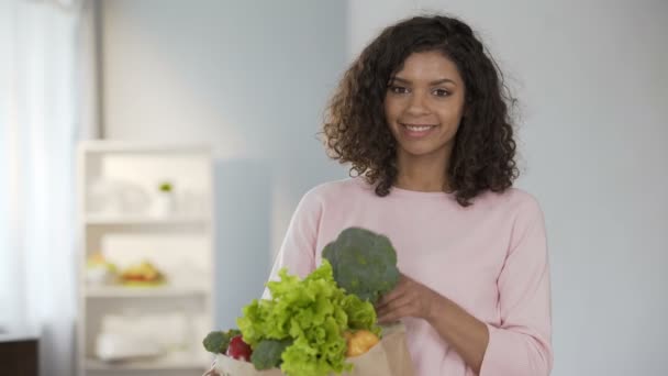 Молодая женщина берет брокколи из продуктовой сумки, улыбается Кэм, здоровый образ жизни — стоковое видео