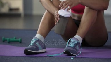 Genç kadın yere, oturma kadar ayakkabı bağcığı bağlama protein kokteyl, içme