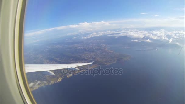 Ala de avião voando alto sobre o mar e costa, nuvens brancas esparsas na distância — Vídeo de Stock
