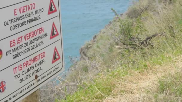 Prohibición multilingüe y señal de advertencia en la cima de una colina cubierta de hierba sobre la costa del mar — Vídeo de stock