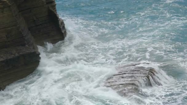 Las olas del mar se rompen en salpicaduras contra acantilados rocosos creando espuma por costa — Vídeos de Stock