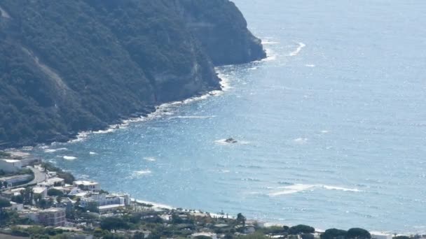 Azurblaues Wellenmeer, das sein Wasser zur Küste mit Bergen wälzt, Oberflächensonne glitzert — Stockvideo