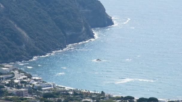 Mare ondulato azzurro rotolando le sue acque verso la costa con montagna, brillantini sole di superficie — Video Stock