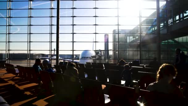 Passageiros sentados em cadeiras no terminal do aeroporto, espaçosa sala de espera iluminada pelo sol — Vídeo de Stock