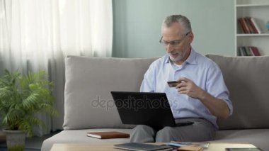 Kanepede oturan ve üzerinde laptop, kartı numarası ekleme emekli online alışveriş