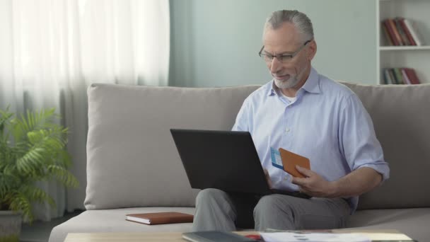 Satisfait vieil homme réservation chambre d'hôtel sur ordinateur portable, tenant passeport et billets — Video