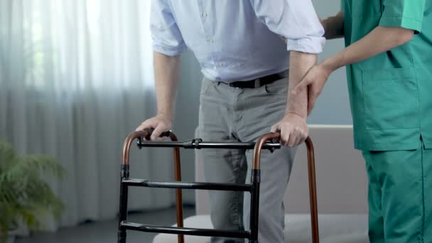 Male patient of nursing home moving with walking frame and nurse, support — Stock Video