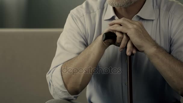 Primo piano di uomo anziano mani tenendo bastone da passeggio, vecchio maschio seduto sul divano — Video Stock