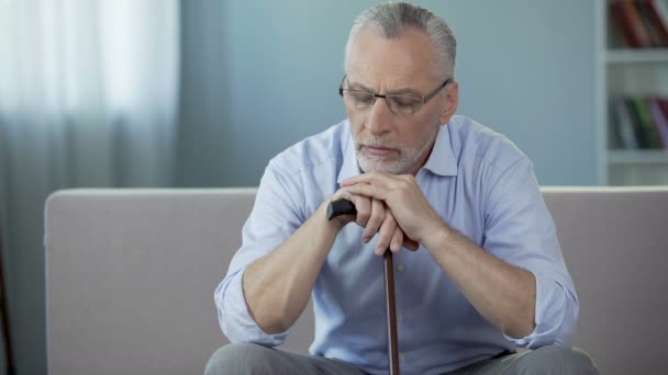 Malo hombre de 50 años sentado en el sofá, poniendo las manos en el bastón. Depresión — Vídeos de Stock