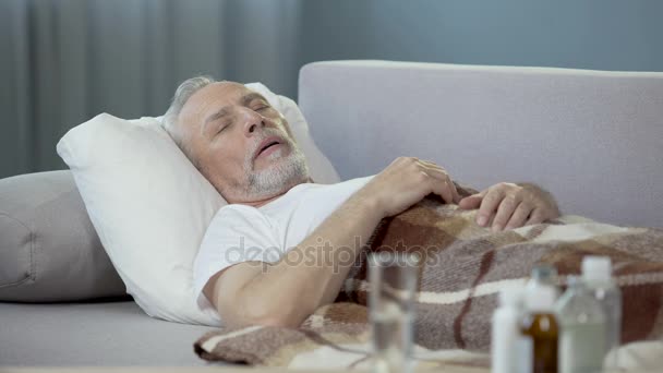 Vieux malade dormant sur le canapé à la maison, médicaments debout sur la table — Video