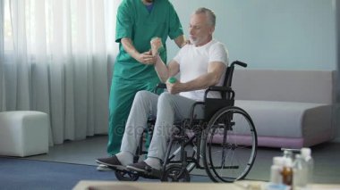 Erkek hemşire, rehabilitasyon yardımıyla zayıf kasları pompalama tekerlekli sandalyede