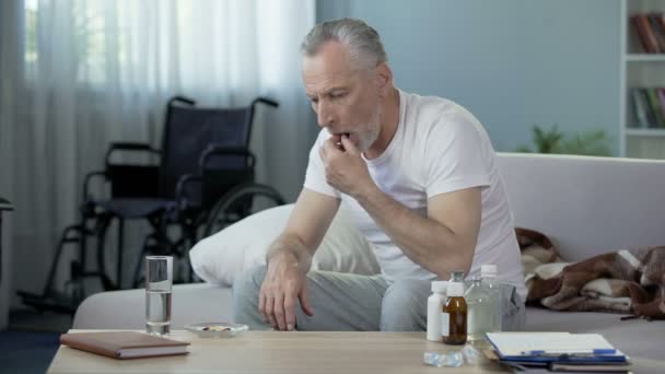 Senior handicapped male sitting on sofa and taking pills, loneliness and sadness — Stock Video