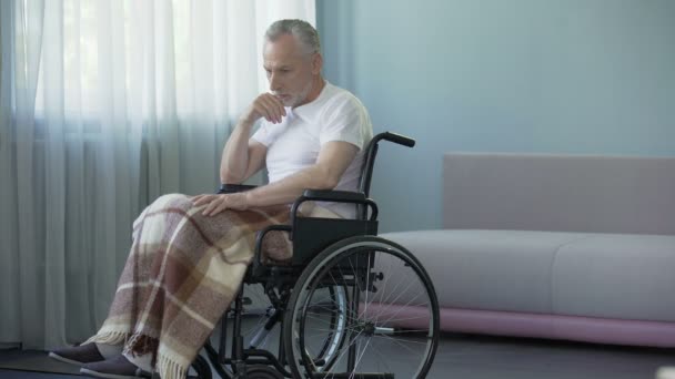 Одинокий старик сидит в инвалидной коляске в больнице, надеется увидеть родственников — стоковое видео