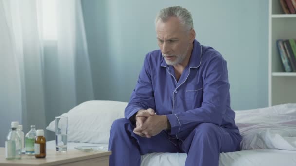 Homem idoso doente perturbado sentado na cama, tomando medicação para se recuperar da doença — Vídeo de Stock