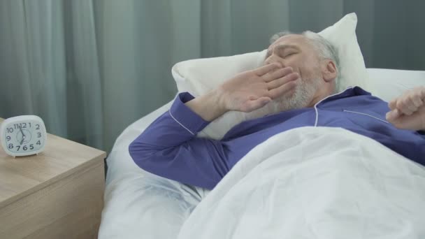 Сповнений сил і енергії чоловік прокидається у своєму затишному ліжку радіючи новому дню — стокове відео