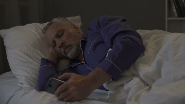 沉迷于智能手机高级男子滚动应用程序, 而不是睡觉 — 图库视频影像