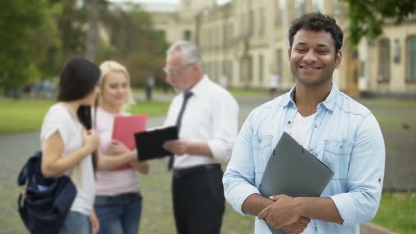 Estudiante hispano feliz de pie cerca de la universidad y mirando a la cámara, educación — Vídeos de Stock