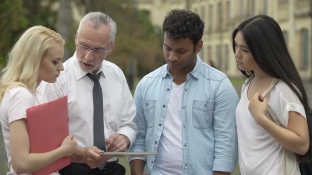 Professor explicando como escrever pesquisa científica, mostrando exemplos em tablet — Vídeo de Stock