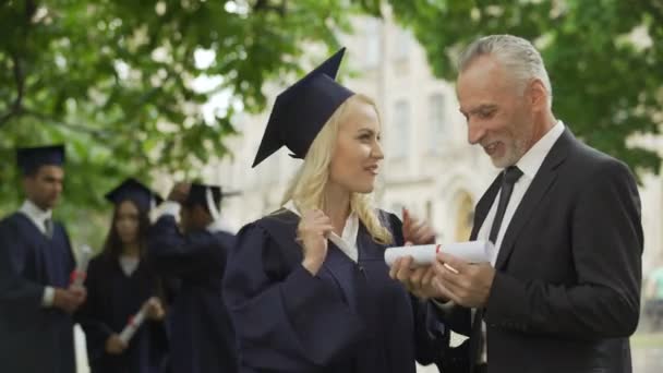 Gelukkig blond afgestudeerde student vreugde diploma met vader, graduatie ceremonie — Stockvideo