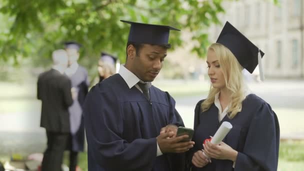 Jongeren in graduate uniforme kijken telefoon scherm, discussie, job — Stockvideo