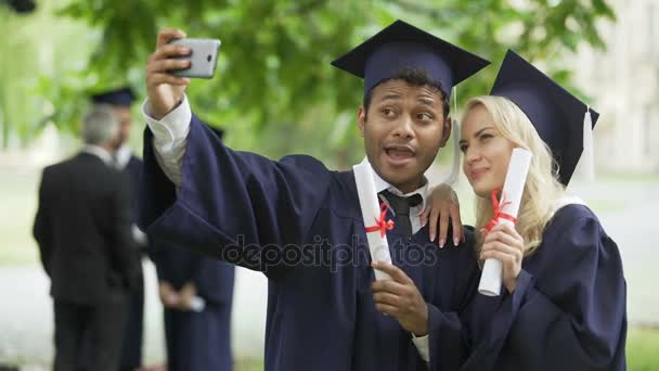 Junge Leute im Abschlussoutfit machen ein Selfie mit dem Handy und betrachten es — Stockvideo