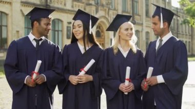Mezun öğrenciler konuşurken ve kameraya bakarak akademik regalia içinde gülümseyen