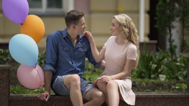 Pessoas apaixonadas sentadas no banco, homem segurando balões, humor romântico despreocupado — Vídeo de Stock
