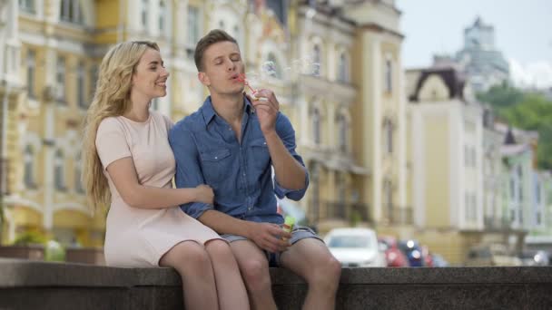 Cara apaixonada fazendo bolhas de sabão, beijando sua namorada sentada ao lado dele — Vídeo de Stock