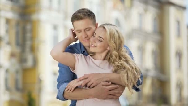 Junger Mann umarmt Freundin von hinten, küsst ihre Hand und Wange, verliebt — Stockvideo