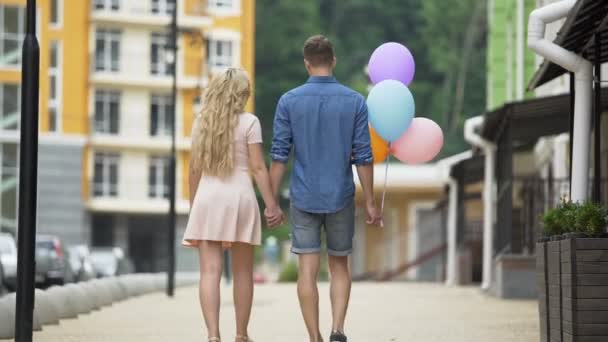 Casal andando rua abaixo de mãos dadas, parando para beijar, cara com balões — Vídeo de Stock
