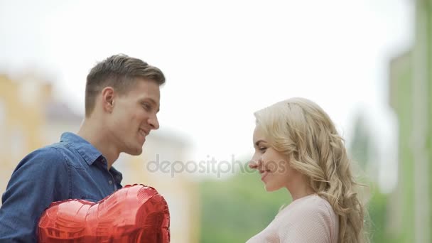 Šťastný pár se blíží navzájem a líbání, schovává za balónky-srdce — Stock video