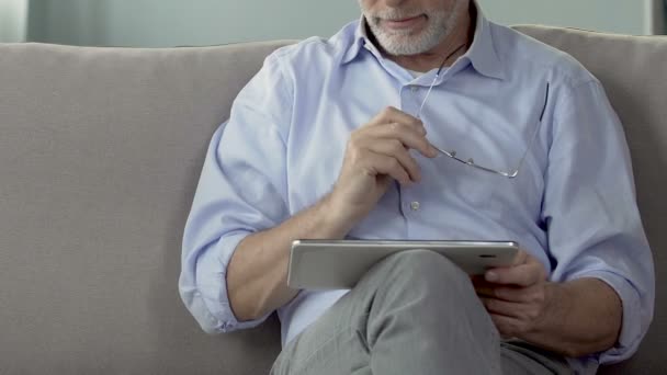 Anciano sosteniendo la tableta en el regazo, planificación y reserva de viaje de jubilación, primer plano — Vídeo de stock
