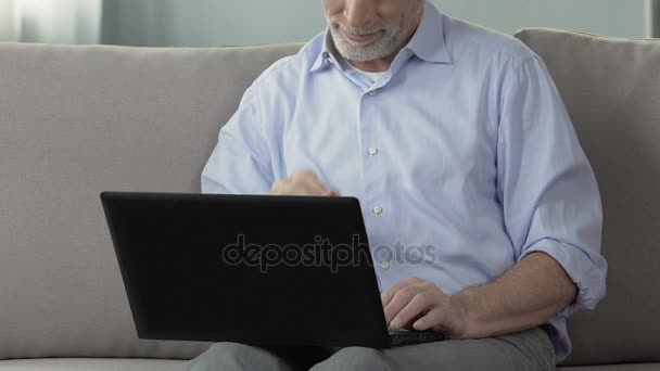 Пожилой человек сидит на диване, используя ноутбук, работает из дома, инженерный проект — стоковое видео