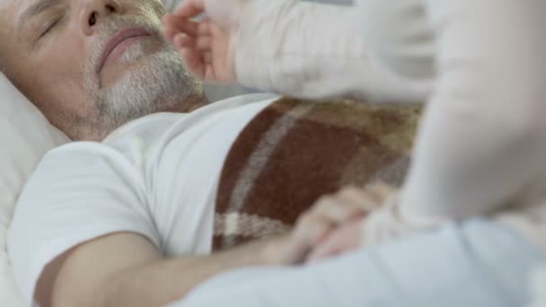 Female sitting on edge of bed, holding old man by hand and taking care of him — Stock Video