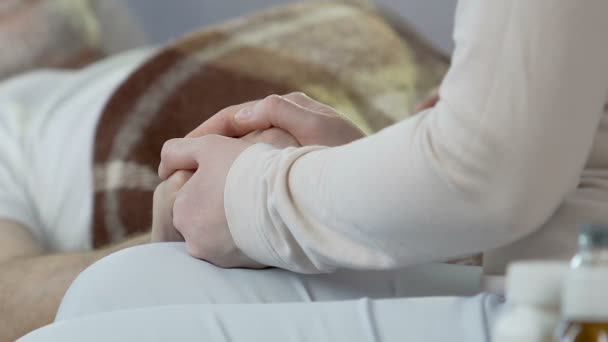 Femme assise sur le bord du lit, tenant à la main un homme âgé, stade terminal, lit de mort — Video